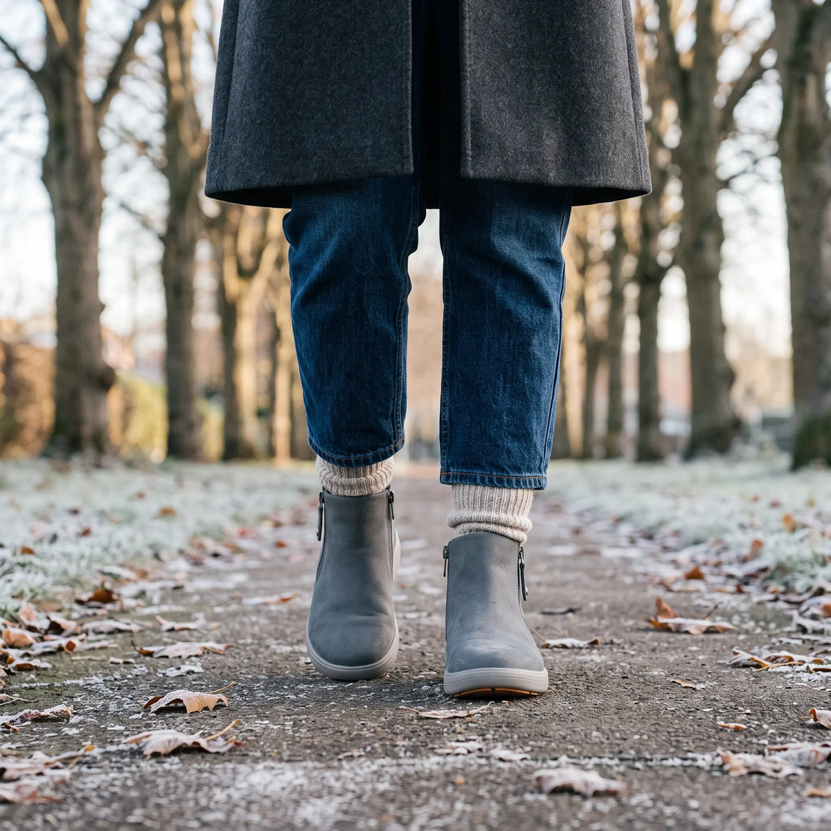 Woman walking in Strive Mayfair grey ankle boots with side zips on a frosty woodland path.