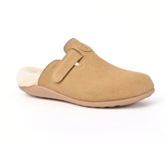 A tan suede clog-style slipper with a soft cream shearling lining and a tan sole, shown from a side profile on a white background. Strive Footwear Oslo II Women’s Tan Slippers