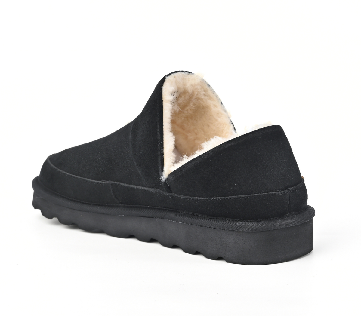 A single black slip-on slipper with a thick black sole and a soft beige shearling lining, shown from a three-quarters angle on a white background. Strive Footwear Women’s Alaska Black Slippers