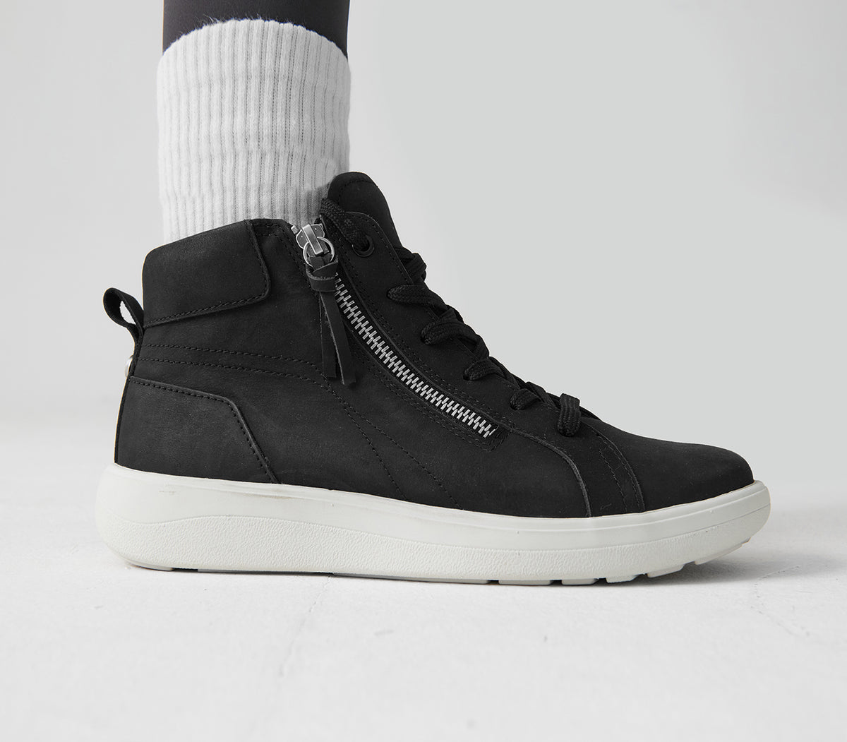 Black high-top sneaker with a zipper on a light gray background. Strive Footwear Women’s Kensington Black Boots 