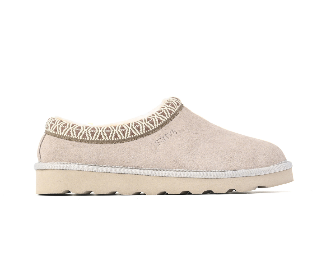 A single slip-on clog-style shoe in light beige suede with a patterned knit collar and a thick cream sole, shown from the side on a white background. The brand name 'STRIVE' is subtly embossed on the side. Strive Footwear Zurich Suede Slippers Grey