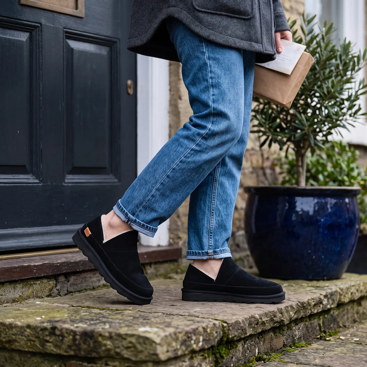 Black Strive Alaska slippers worn with blue jeans while walking down stone steps.