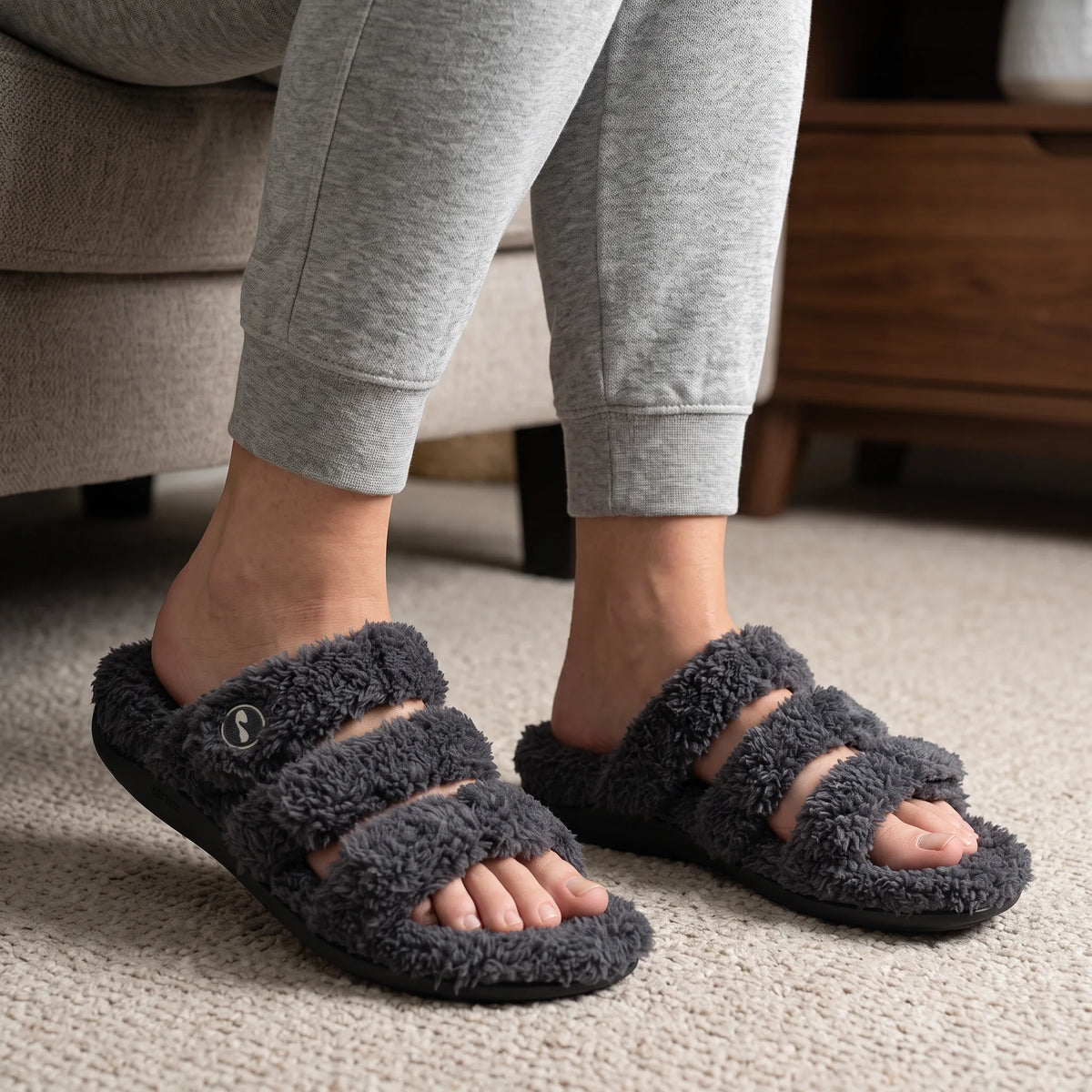 Grey Strive Zella teddy multi-strap slippers worn in a neutral living room.