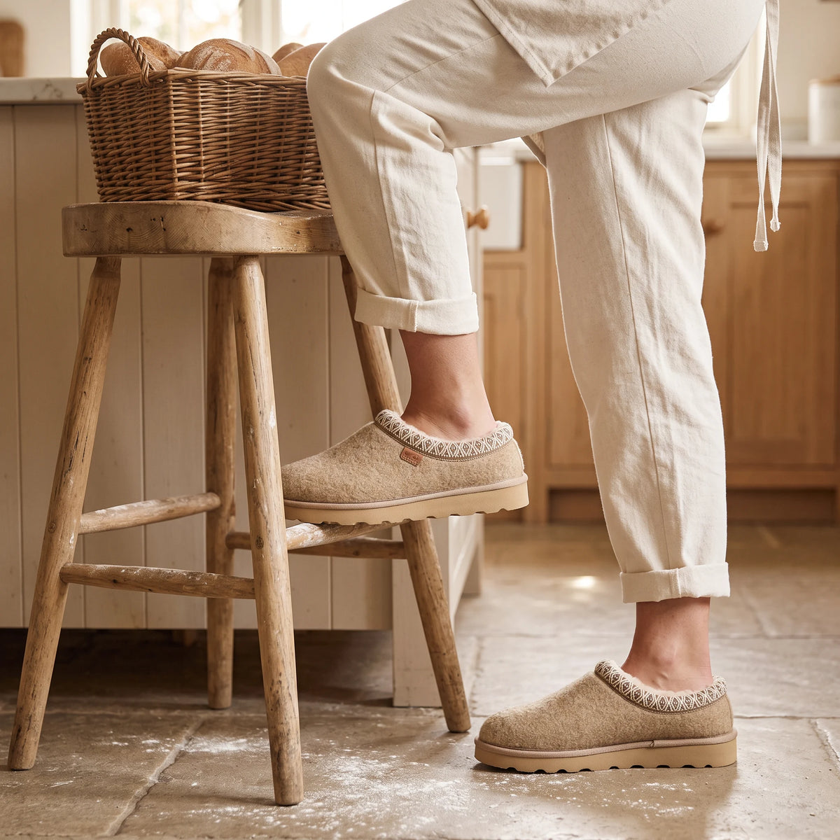 Tan Strive Zurich felt slippers with patterned trim, worn in a warm country-style kitchen.